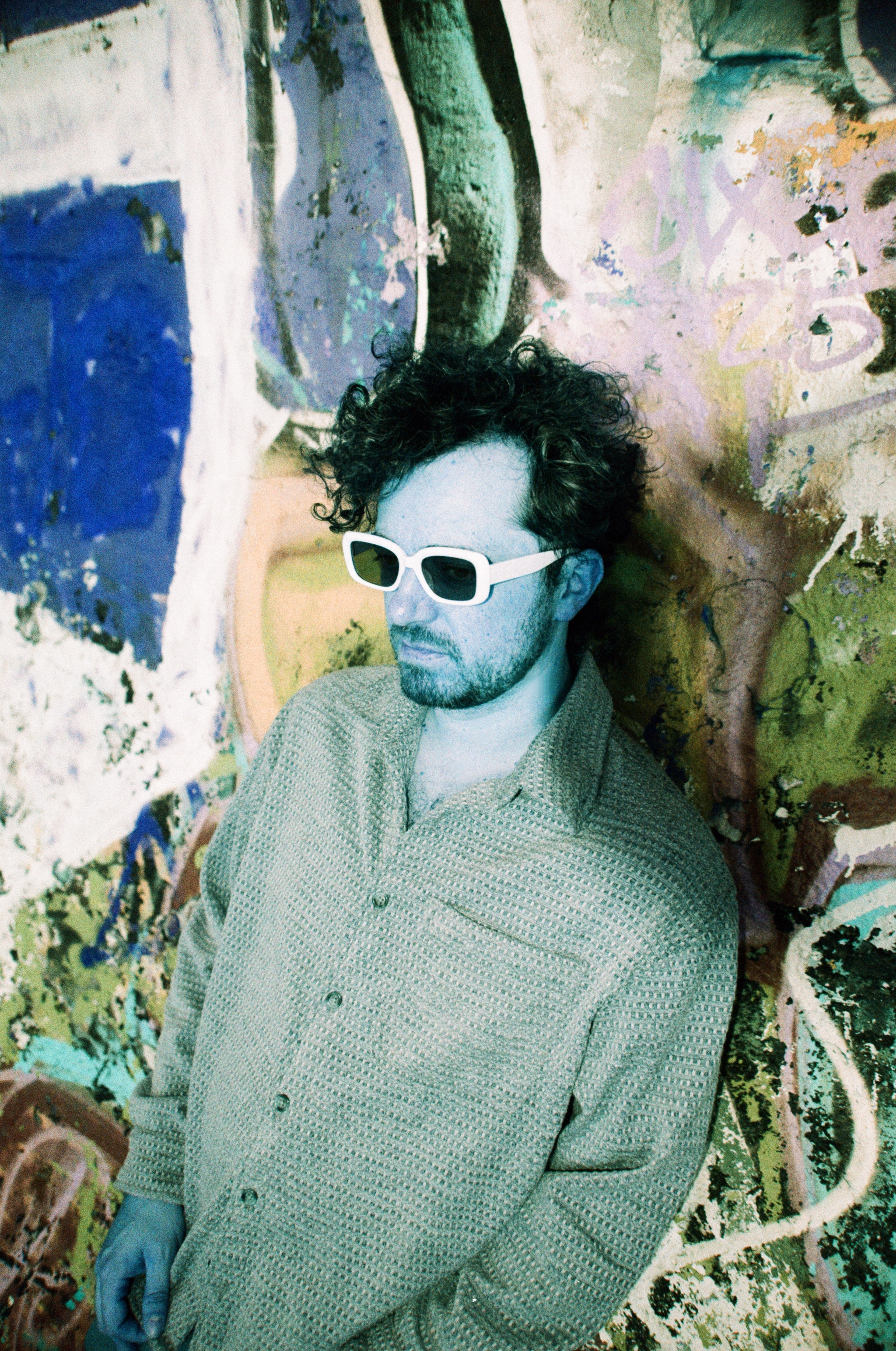 Bloom Ritual songwriter Kevin Stefanescu wearing white sunglasses against a painted wall